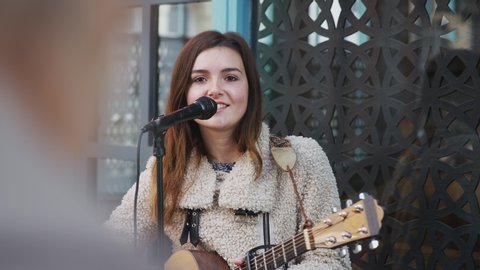 Young woman busking playing acoustic guitar and singing outdoors to crowd in street - shot in slow motion