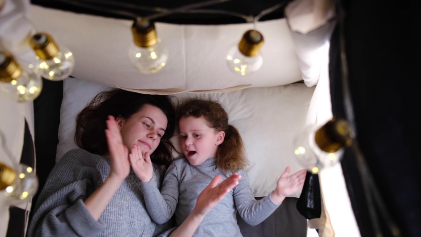 Top view on mom and cute daughter playing patty cake at home, carefree family of mother and little child girl clap hands having fun together laughing enjoying funny game lying down in tent Royalty-Free Stock Footage #1044063826