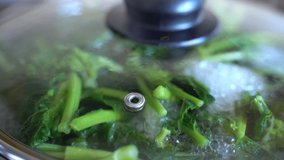 Steaming veggies in cooking pan on kitchen stove, boiling water and fresh spinach steaming inside. Steam and vapour concept, vegetarian food, healthy eating and diet concept