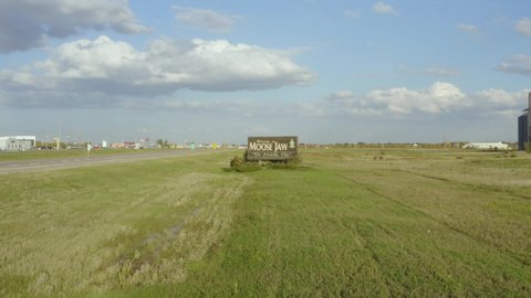 View of field and street sign in Moose Jaw, Saskatchewan, Canada. 4k drone footage,track in above the city billboard, road and prairies. House in the background.