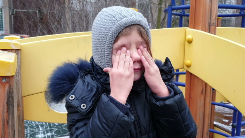 close up view of little girl rubbing her eyes with her hands and crying on playground in the fall