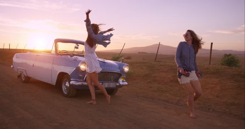 Girl friends dancing at sunset on road trip with vintage car RED DRAGON