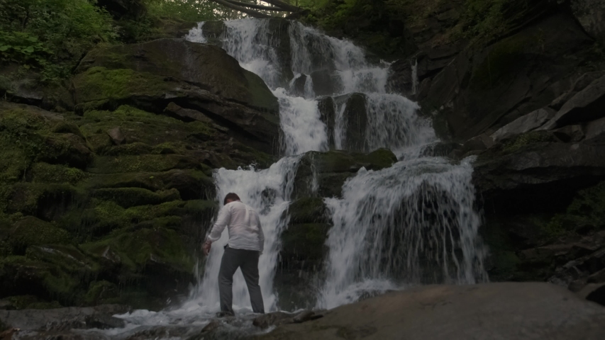 A man comes under a large waterfall. Ritual cleansing. 4k. Slow motion