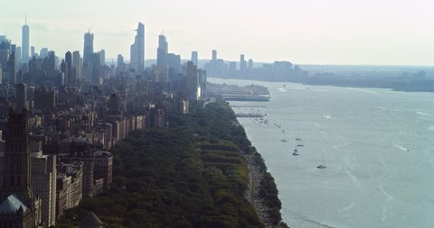 Aerial view of Manhattan greenery and skyscrapers next to river in New York during the day under overcast blue sky. Wide shot on 4K RED camera.