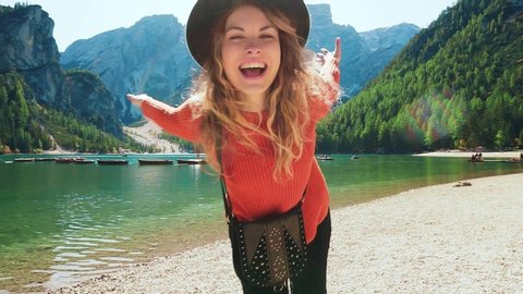 active happy joyful fun young tourist woman smile face walks. Bright summer nature landscape Dolomites Alps Italy. enjoying vacation lake Braies. runs to camera raised open arms hands. Girl model hat