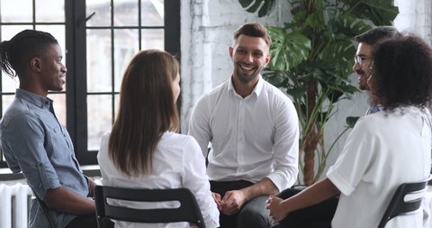 Smiling male coach psychologist talk to diverse people patients group sit in circle at therapy session, counselor therapist help with problems at psychotherapy rehab meeting business training concept