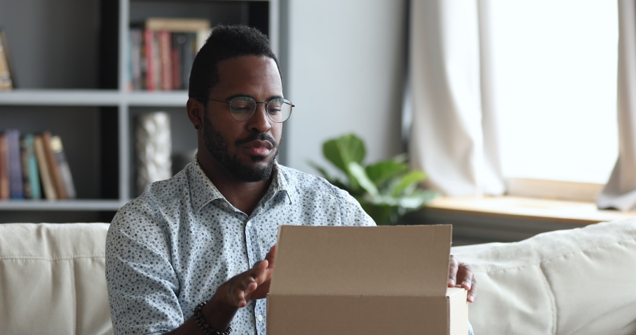 Frustrated dissatisfied african man customer open cardboard box receive damaged wrong parcel, disappointed male consumer having problem with bad fake online shop post shipping delivery order concept Royalty-Free Stock Footage #1044100471