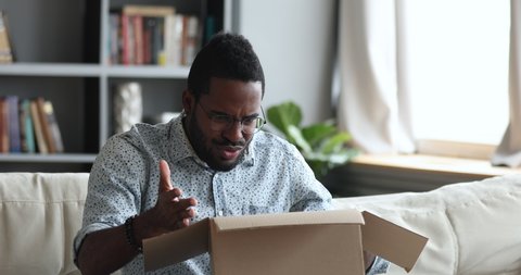 Frustrated dissatisfied african man customer open cardboard box receive damaged wrong parcel, disappointed male consumer having problem with bad fake online shop post shipping delivery order concept