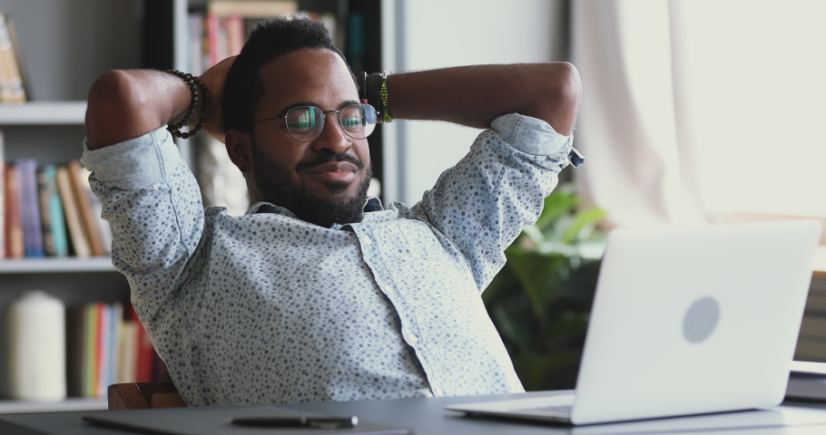 Happy young african businessman worker student relaxing sit at office desk hold hands behind head looking at laptop screen watch webinar online videos on computer resting at workplace finished work. Royalty-Free Stock Footage #1044100507