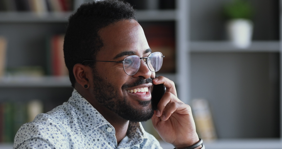 Smiling young adult mixed race professional casual businessman making business call talking on the phone in office, happy afro american salesman enjoying mobile conversation indoors, close up view Royalty-Free Stock Footage #1044100516