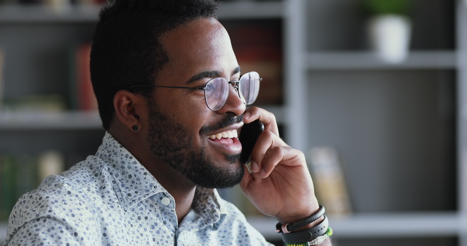 Smiling young adult mixed race professional casual businessman making business call talking on the phone in office, happy afro american salesman enjoying mobile conversation indoors, close up view Royalty-Free Stock Footage #1044100516
