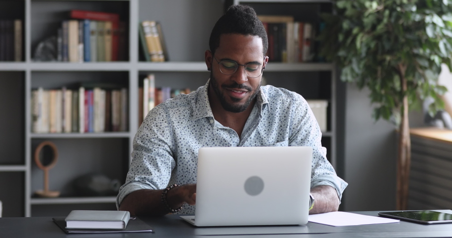Happy african man student worker make notes study work on laptop, young male professional watch educational video webinar course distance e learn with online teacher concept sit at home office desk Royalty-Free Stock Footage #1044100558