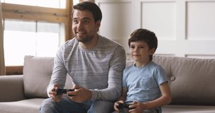 Overjoyed young adult dad and cute child son gamers winners playing winning video game, excited father having fun with kid boy give high five holding celebrating videogame victory at home