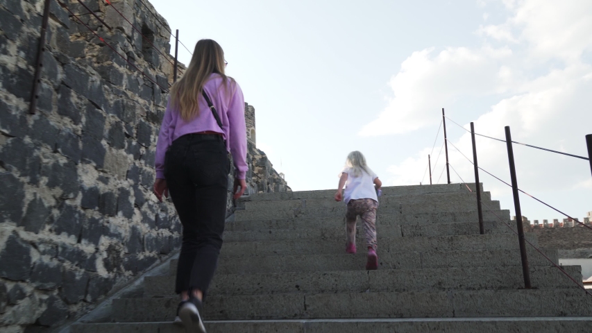 Young mother with two little daughters climbing on a wall of medieval castle