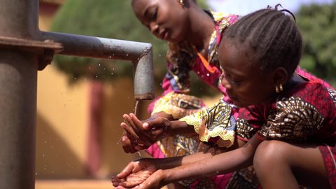 Two beautifully Dressed Little African Girls Sipping Water From a Tap
