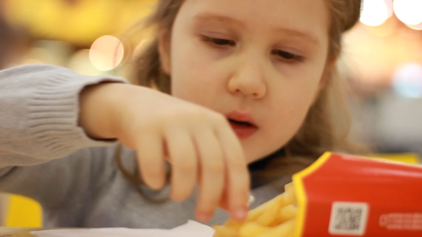 Child girl eating fast food french fries in a cafe Mcdonalds. Portrait closeup. Royalty-Free Stock Footage #1044122923