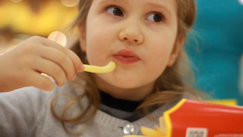 Child girl eating fast food french fries in a cafe Mcdonalds. Portrait closeup.