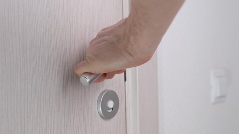 Men's hand opens wooden door in white room. Close up.