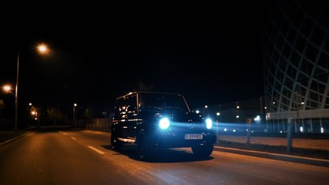 Bucharest, Romania - 10.20.2019: Crane rolling shot of a Mercedes G Klasse luxury SUV car driving on a city street at night 
