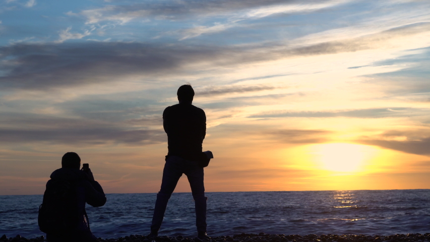 A man is photographed at sunset near the sea.