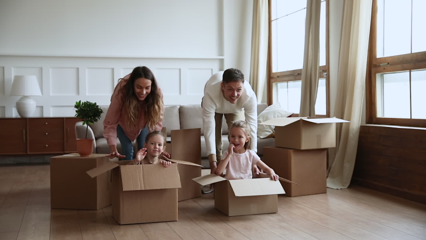 Excited happy young parents run push cardboard boxes with little cute children daughters ride inside, family homeowners playing having fun on moving day celebrate mortgage relocation removals concept | Shutterstock HD Video #1044147325