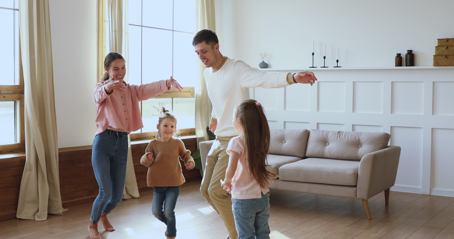 Happy active family young adult parents mum dad and cute little children daughters holding hands dancing jumping together in living room interior enjoying funny weekend activity in modern apartment Royalty-Free Stock Footage #1044147328