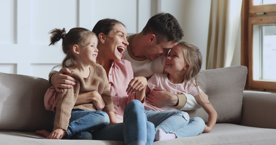 Happy loving family or four laughing hugging cuddling relaxing on sofa, affectionate adult parents and cute little kids children daughters having fun embracing bonding enjoying tender moments at home Royalty-Free Stock Footage #1044147397