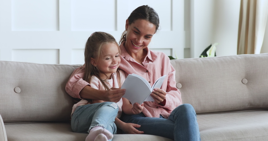 Caring single parent young mother babysitter hug happy cute little preschool child girl kid daughter hold learn read book fairy tale story bonding enjoying family lifestyle hobby at home sit on couch | Shutterstock HD Video #1044147403