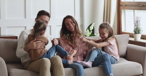 Cheerful loving family young adult parents and cute small kids siblings having fun cuddling tickling playing on sofa in living room, young couple enjoying leisure game with little children on couch