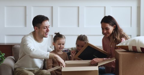 Excited family with two cute little kids daughters unpacking boxes sit on sofa in new apartment on moving day, young parents and small children customers open parcels buying home furnishings concept