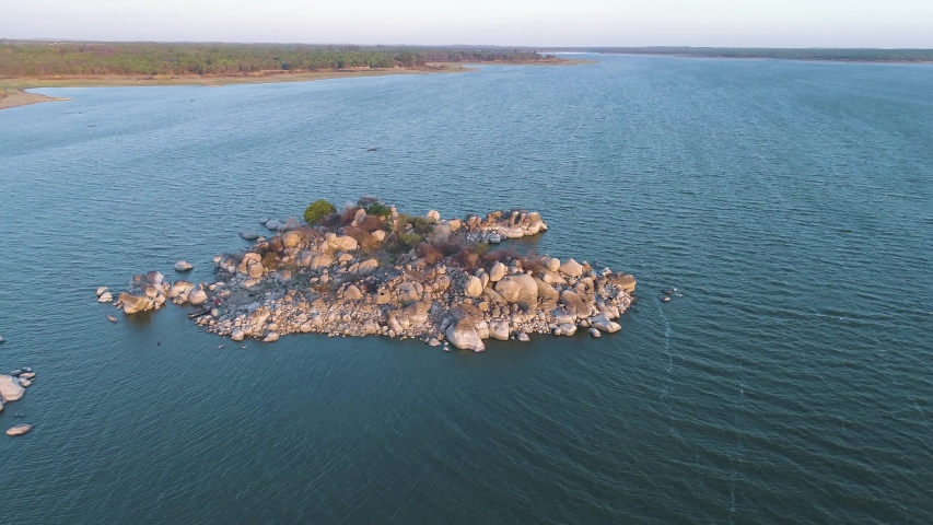 Aerial, drone footage of a rocky island in Lake Chivero, lit by the setting sun. Tourist place near Harare, Zimbabwe, Africa.