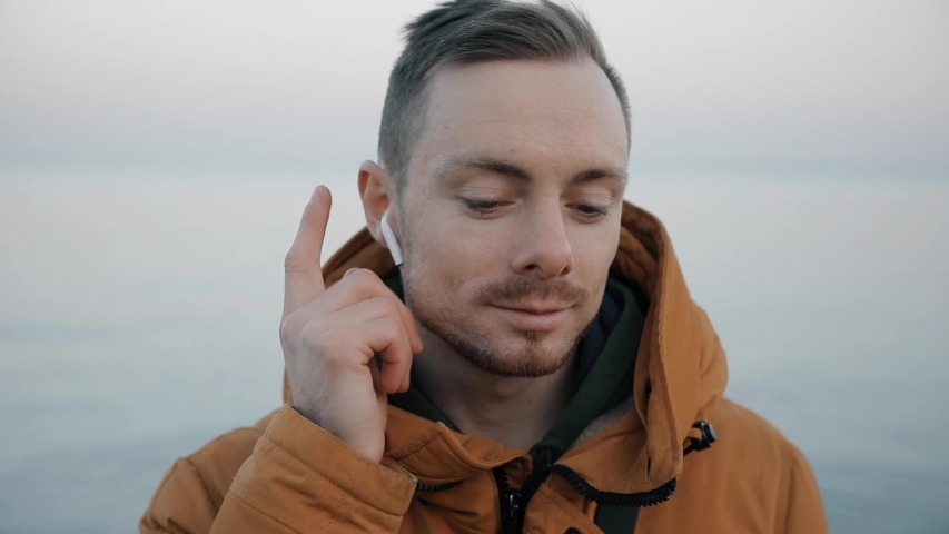 Man listening his playlist touching wireless earphones changing sound track at the sea beach