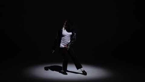 Young stylish man dancing in style Michael Jackson, spotlight on a black background.
