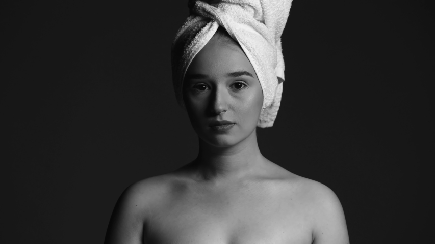 Black and white portrait of gently girl in a towel looking at the camera on a black background. Close up