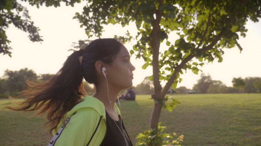 An attractive girl jogger jogging in a park with her earphones on.  A fitness enthusiast female runner running in the morning while listening to music.