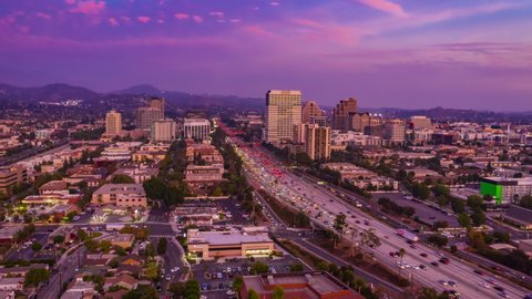 Aerial time lapse in motion of a beautiful golden hour red sunset over Los Angeles city in California with freeway and cars below.