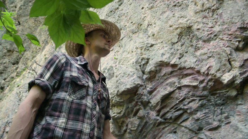 Young man in hat walks barefoot along mountain forest road, looks up. Summer.