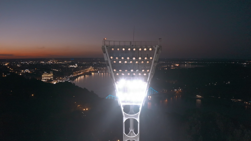 Switching on the light tower of a football stadium against a sunset and a night city cinematic smooth movement of a drone