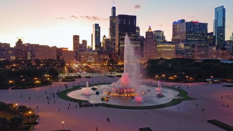 Aerial: Tourists at Buckingham Fountain in Grant Park at sunset. In the background is the Chicago City Skyline. 