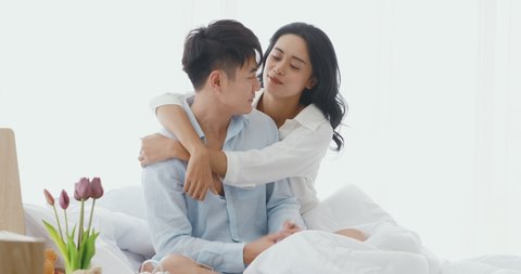 Lovely Asian couple sitting on bed. Woman trying to kiss her boyfriend's cheek. Man try to avoid her in bedroom. This is a lover time.
