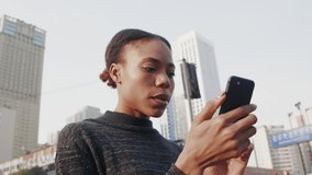 Slow motion one happy young African woman typing on mobile phone in the street pretty low angle view of black girl using looking at her smartphone in urban city young people lifestyles 4k clip