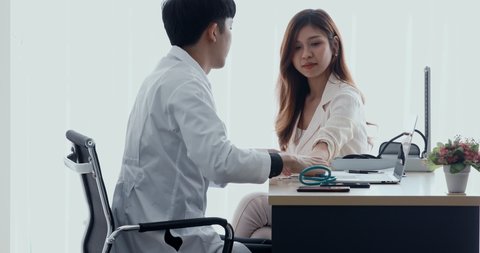 Asian doctor using the stethoscope to check the female patient's pulse.
