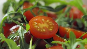Pouring olive oil on salad with cherry tomato and rukkola, slow motion video