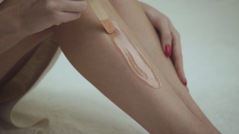 Waxing female legs with wooden stick in spa.