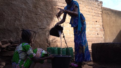 African Teenage Girl Pouring Water Into A Big Rubber Bucket