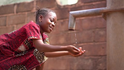 Happy Little African Girl Drinking Water At The Village Pump Station