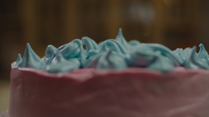 Rotating pink cake with blue decorated meringue flower in slow motion with blurred background lights. 