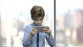 Handsome boy playing video game on smartphone. Cute child using mobile phone, front view. Children, leisure, technology, internet, lifestyle.