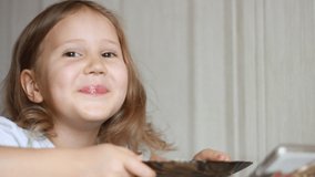 Child eats soup with a spoon and and looks video on a smartphone. Closeup baby girl sitting at the table of home cooking and eating food.
