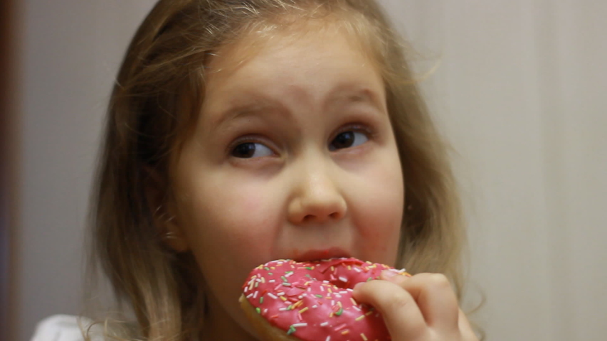 Child mouth bites rose donut. Closeup baby girl eating doughnut with glase. Delicious, sweet, sweettooth.